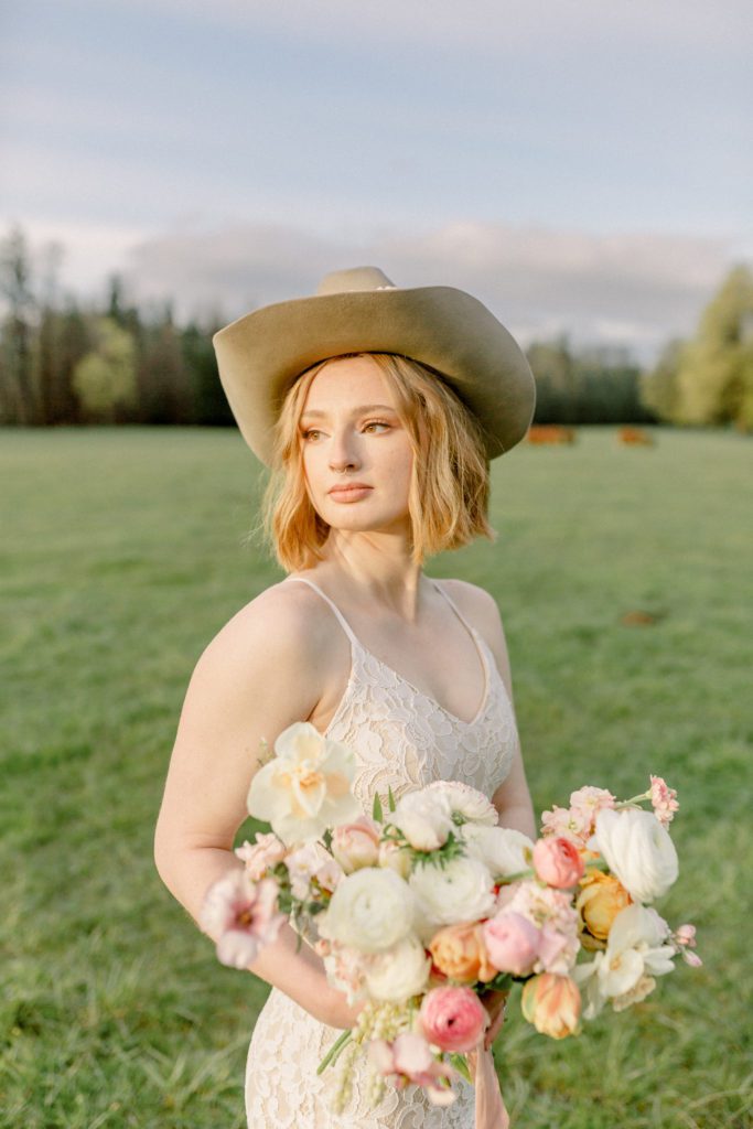 Bride holds spring bouquet & looks  off into the distance with cowboy hat on. 