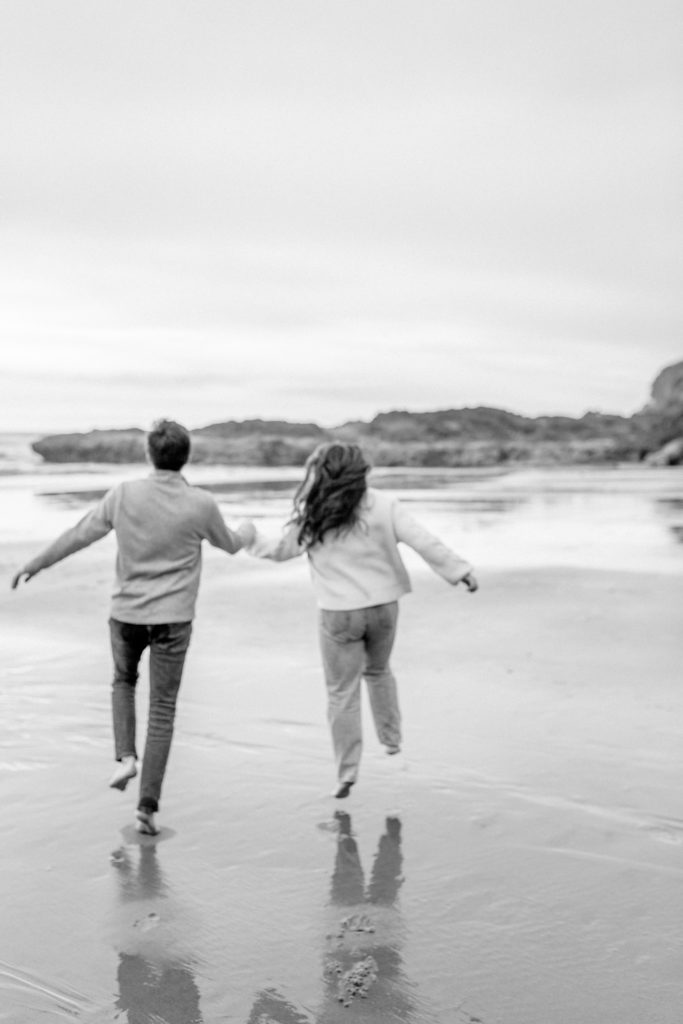 A couple hold hands and run towards the ocean on the oregon coast