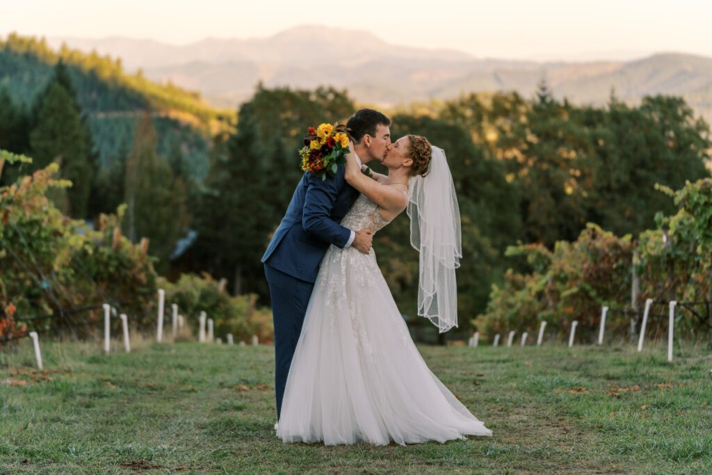 newlyweds kiss in the vineyard at sunset at spire mountain cellars